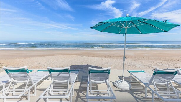 Ein Strand mit weißen Liegestühlen und einem grünen Sonnenschirm.