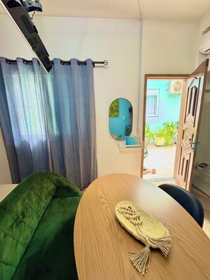 A room with a green sofa, a wooden table with a woven placemat, a mirror, and a view of the outside. - Prado Guest House (Florianópolis)