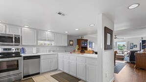 A modern kitchen with white cabinets, stainless steel appliances, and a wooden dining area. - Seaward B103 (New Smyrna Beach)