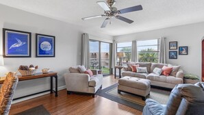 A spacious living room with a ceiling fan, large windows, and a balcony. - Seaward B103 (New Smyrna Beach)