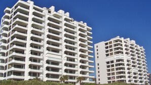 A high-rise hotel with multiple balconies, located near a beach.