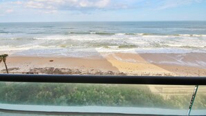 A beach view from a balcony with a railing, ocean waves, and a clear sky.