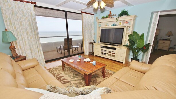 A living room with a large window, a wooden coffee table, beige sofas, and a television on a cabinet.