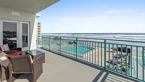 A balcony with wicker furniture, a glass-top table, and a view of the ocean. - The Wave 302 (New Smyrna Beach)