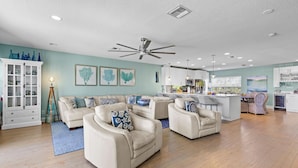 Uma sala de estar espaçosa com um grande ventilador de teto, uma área de cozinha e um espaço para refeições.