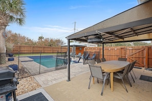 An outdoor patio with a pool, covered seating area, and a grill. - Poolside Oasis (New Smyrna Beach)