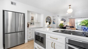Una cocina moderna con electrodomésticos de acero inoxidable, armarios blancos y tiradores dorados.