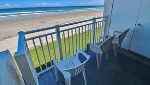 A balcony with a view of the beach, a door, and two chairs.