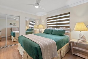Ein Schlafzimmer mit einem großen Bett, einem Spiegel, einem Deckenventilator und einem Nachttisch mit einer Lampe.