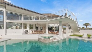 Una casa moderna con piscina, un porche cubierto y un balcón de dos pisos.