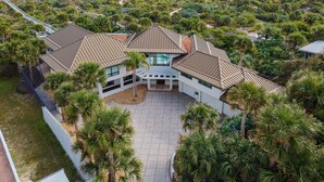 Una casa grande y moderna con un patio amplio y varios niveles de techo, rodeada de exuberante vegetación y vistas al océano.