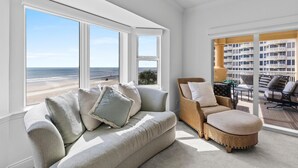 Ett vardagsrum med utsikt över stranden, en flätstol och en balkong med ett räcke.