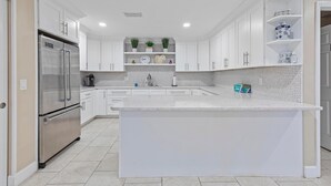 A modern kitchen with white cabinetry, a stainless steel refrigerator, and a central island. - Errol by the Sea 515 (New Smyrna Beach)
