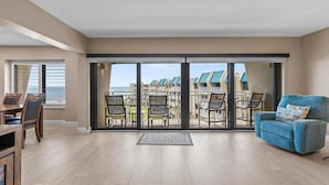 A spacious living room with a large sliding glass door leading to a balcony with outdoor furniture. - Errol by the Sea 515 (New Smyrna Beach)