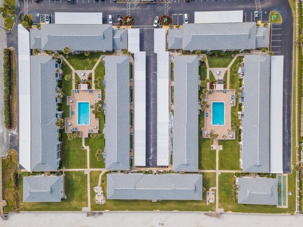 An aerial view of a hotel with multiple buildings, each with a swimming pool and outdoor seating areas.
