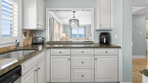 A kitchen with white cabinets, granite countertops, a built-in dishwasher, and a hanging light fixture.