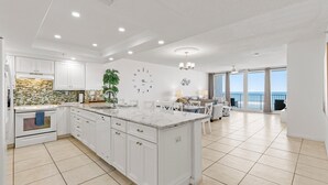 Une cuisine spacieuse avec des meubles blancs, un grand îlot central et une vue sur l’extérieur.