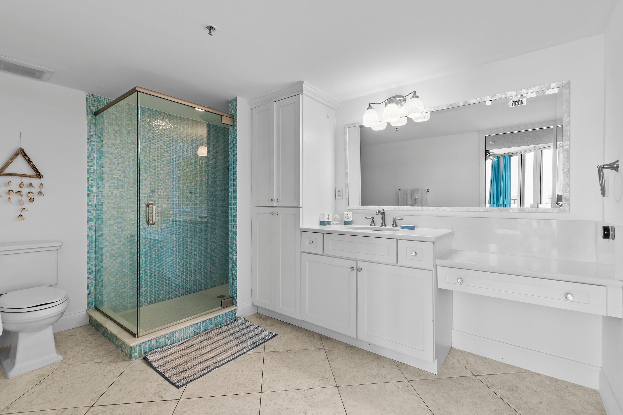A modern bathroom with a glass-enclosed shower, white cabinetry, and a large mirror with lights.