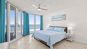 Une chambre avec un lit, une table de chevet, un ventilateur de plafond et une vue sur l’océan grâce à de grandes portes-fenêtres coulissantes.