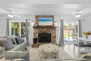 A living room with a stone fireplace, a television, a sofa, and a dining area. - Barefoot Bungalow (New Smyrna Beach)