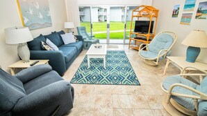 A living room with a sofa, armchairs, a coffee table, and a patterned rug. - Surfside 107 (New Smyrna Beach)