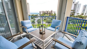 A balcony with four blue cushioned chairs and a wooden table, overlooking a well-maintained garden and buildings. - Oceanwalk 1-501 (New Smyrna Beach)