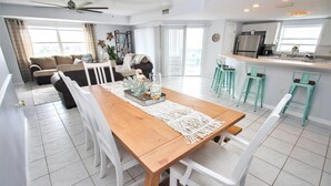 A spacious dining area with a wooden table, white chairs, and a macrame runner. - Oceanwalk 1-501 (New Smyrna Beach)