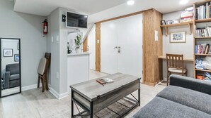 A modern living room with a grey sofa, a wooden coffee table, a bookshelf, and a television mounted on the wall. - DC Guest Suite Walkable, Parking, Pets Welcome (Washington)