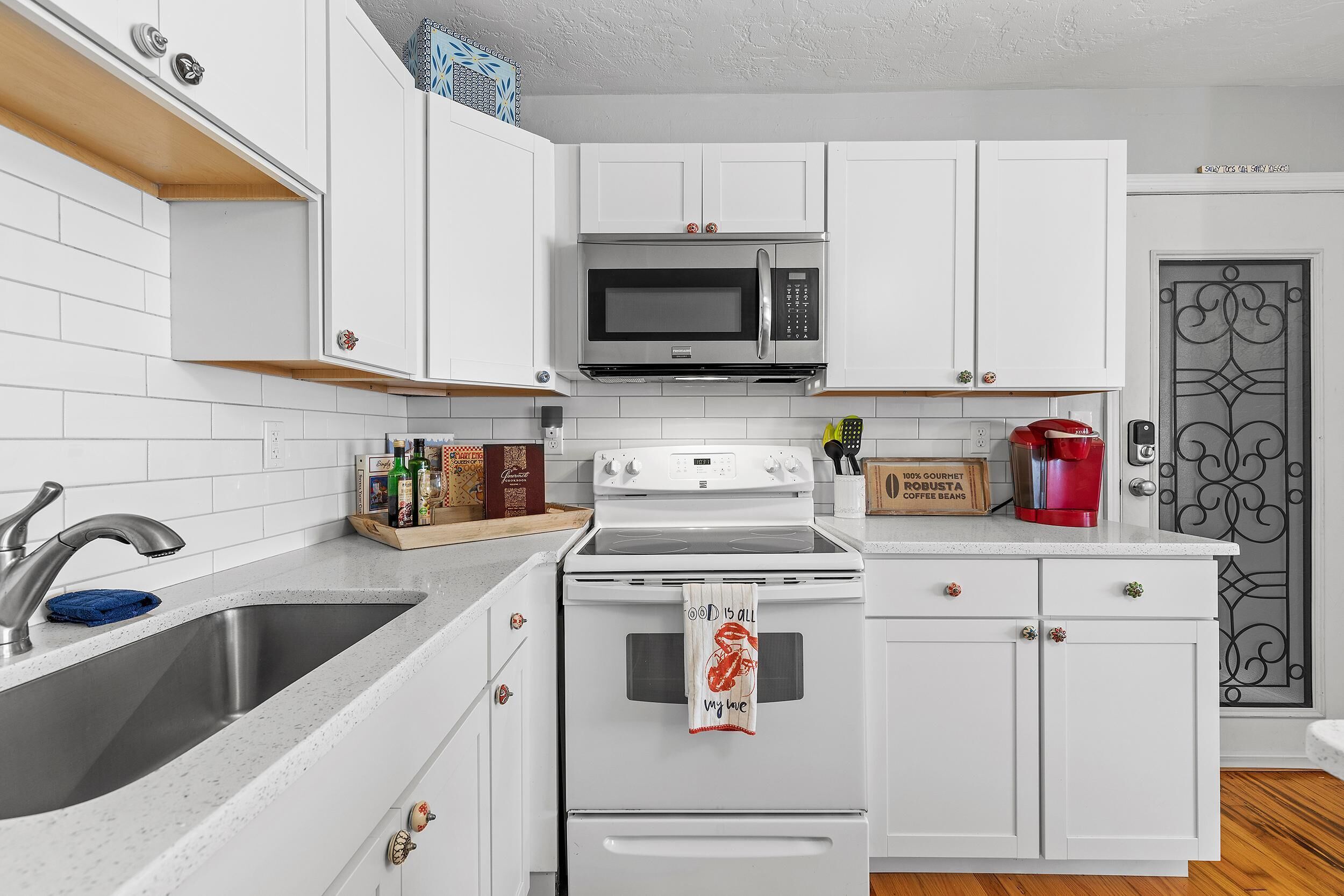 Una cocina con armarios blancos, un lavamanos de acero inoxidable, un microondas y una estufa.