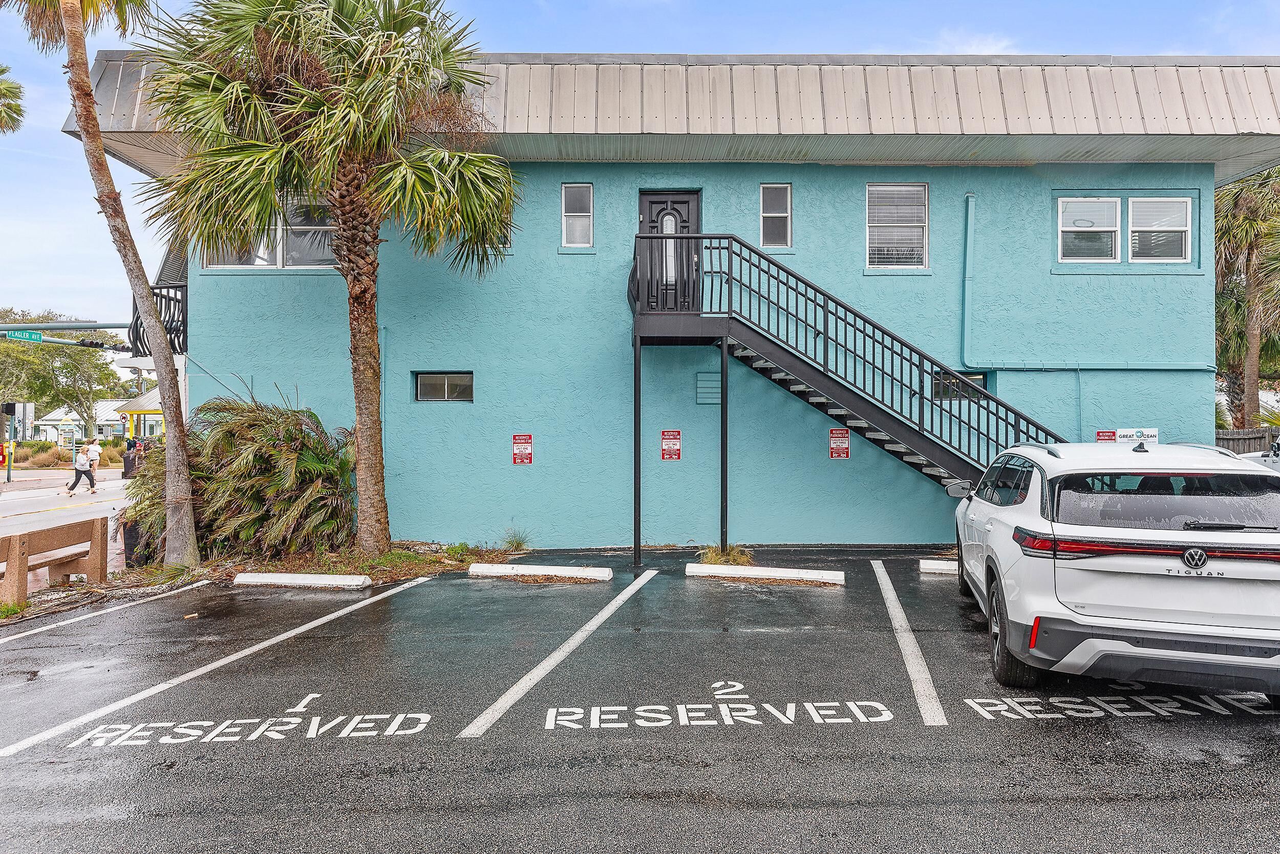 A building with a blue exterior, a staircase leading to a door, and a white car parked in a reserved parking space.