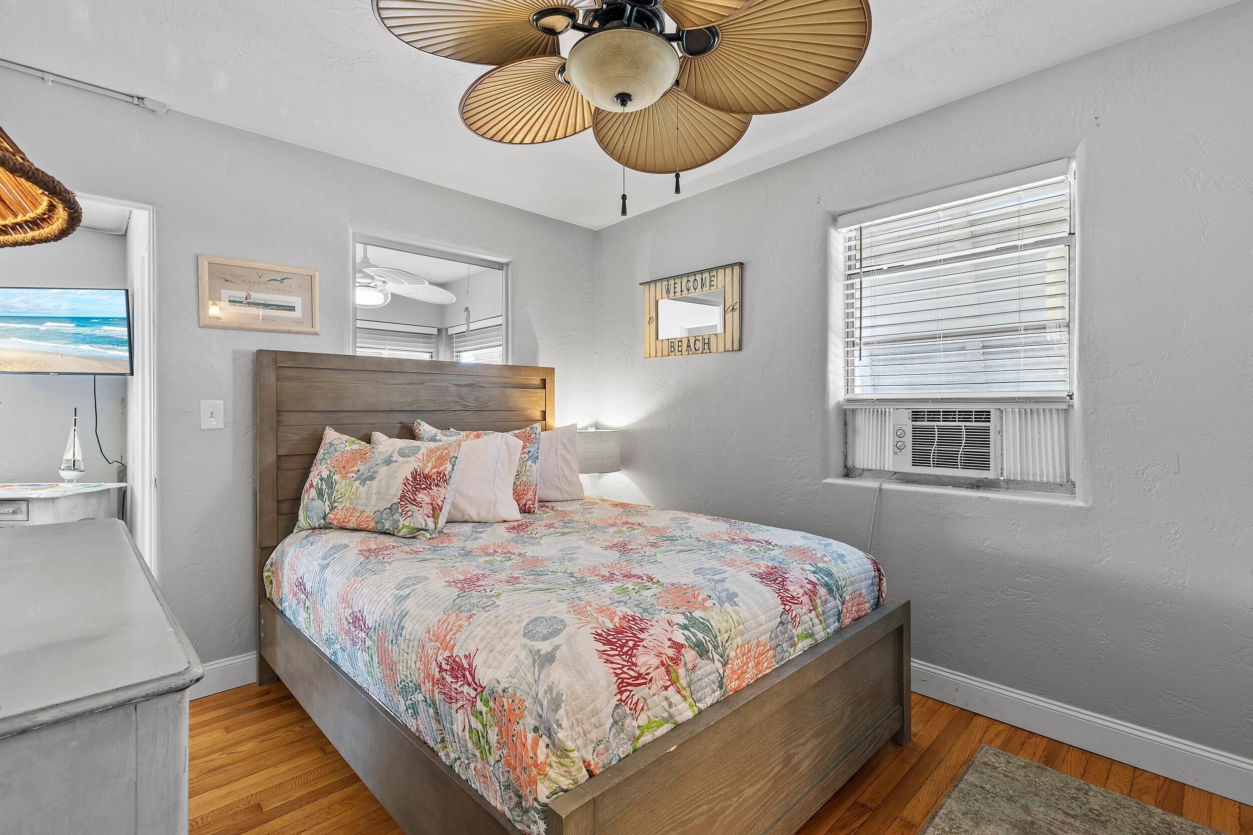 Quarto com cama de madeira, ventilador de teto, janela com persianas e ar condicionado fixado na parede.
