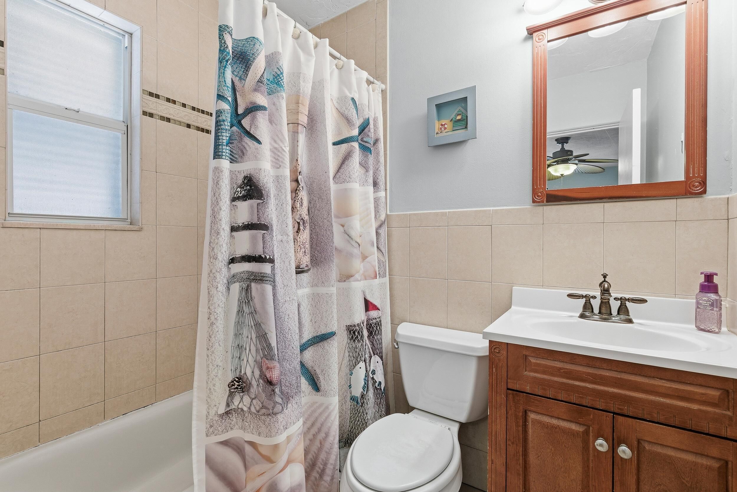 Un baño con cortina de ducha, inodoro, lavabo, espejo y un pequeño cuadro en la pared.