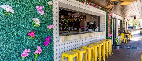 A restaurant with a green wall adorned with flowers, a bar counter, and yellow stools.