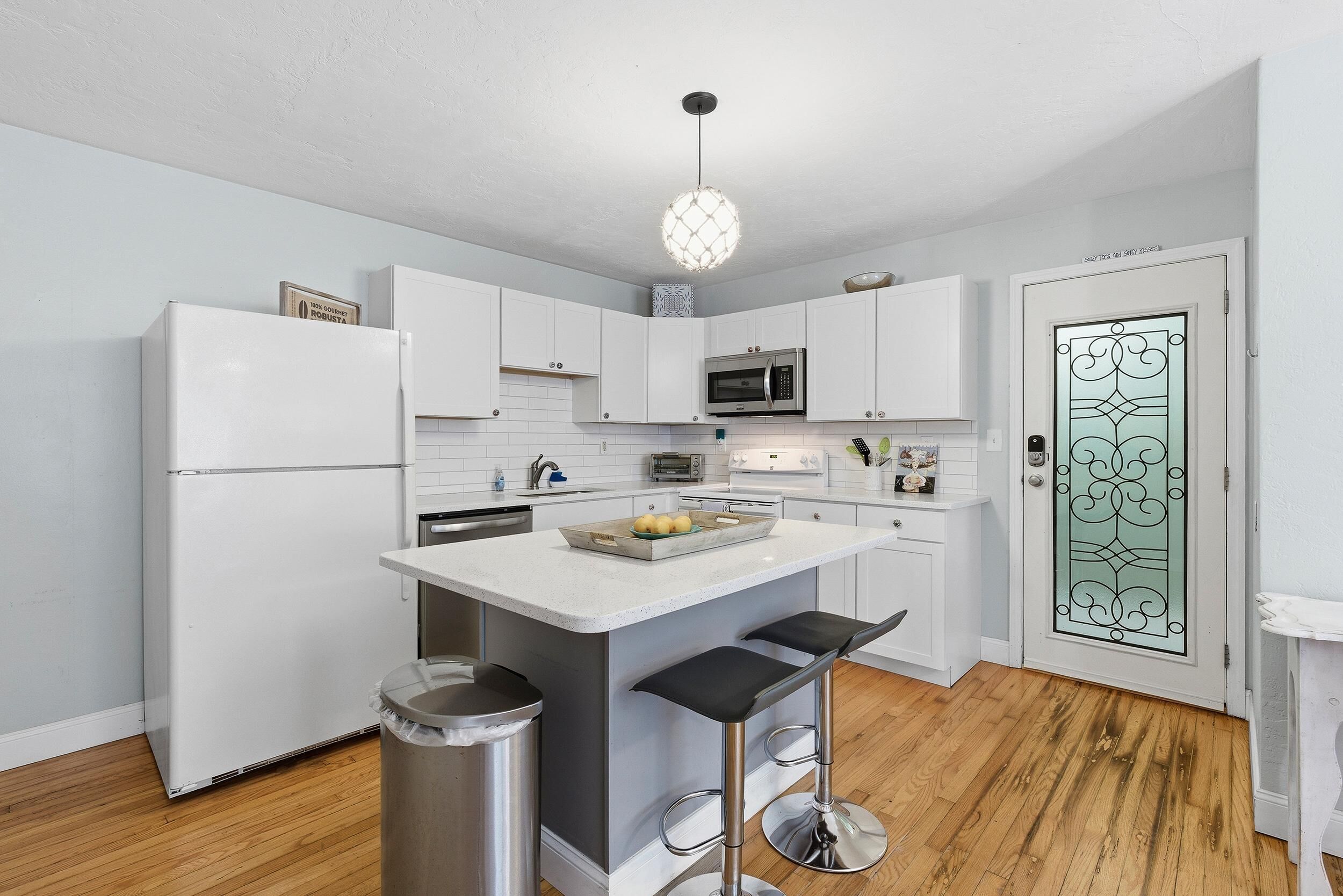 Een moderne keuken met witte kasten, een centraal eiland met krukken, een roestvrijstalen koelkast en een decoratieve glazen deur.