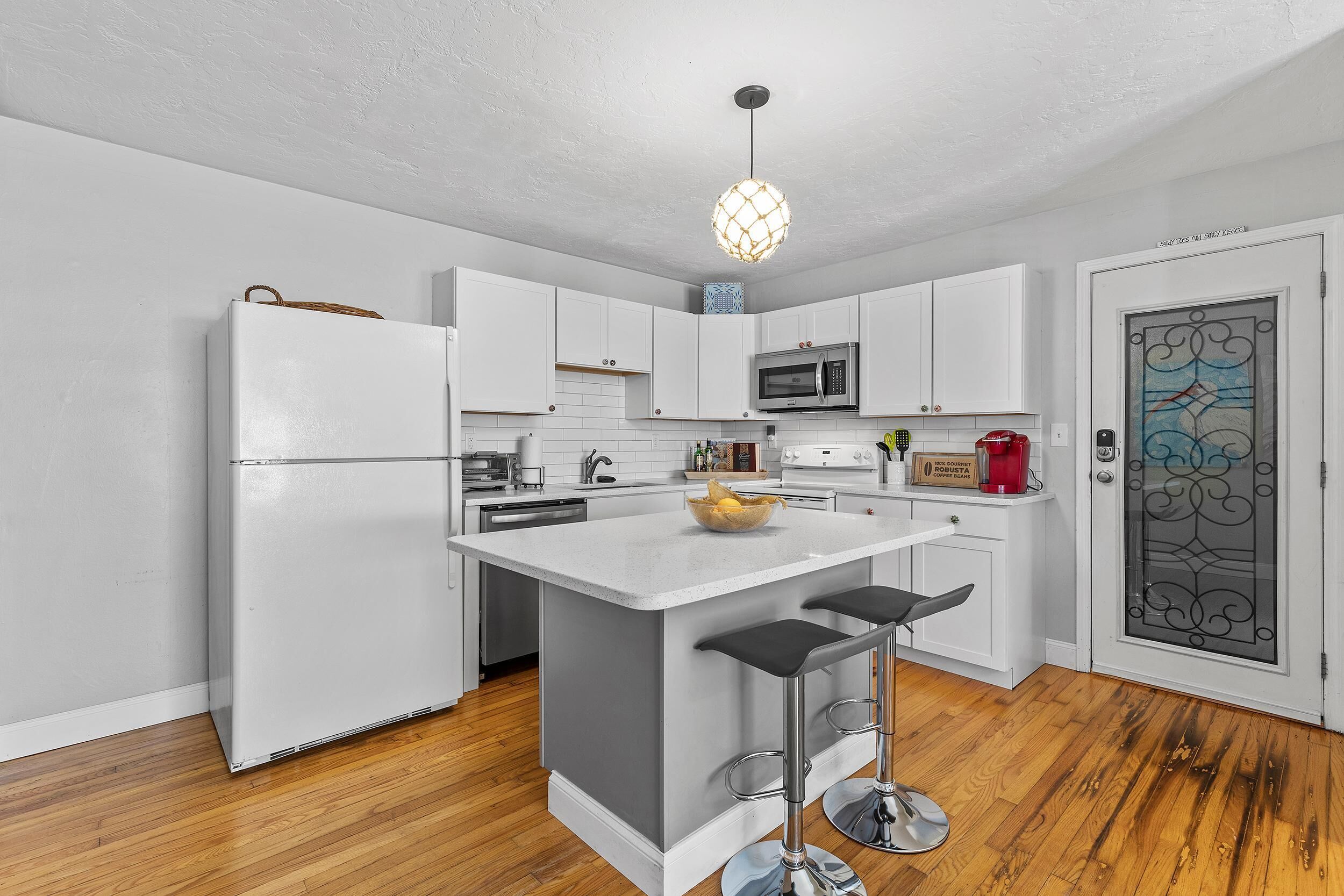 A modern kitchen with white cabinets, a central island with stools, a microwave, and a hanging light fixture.