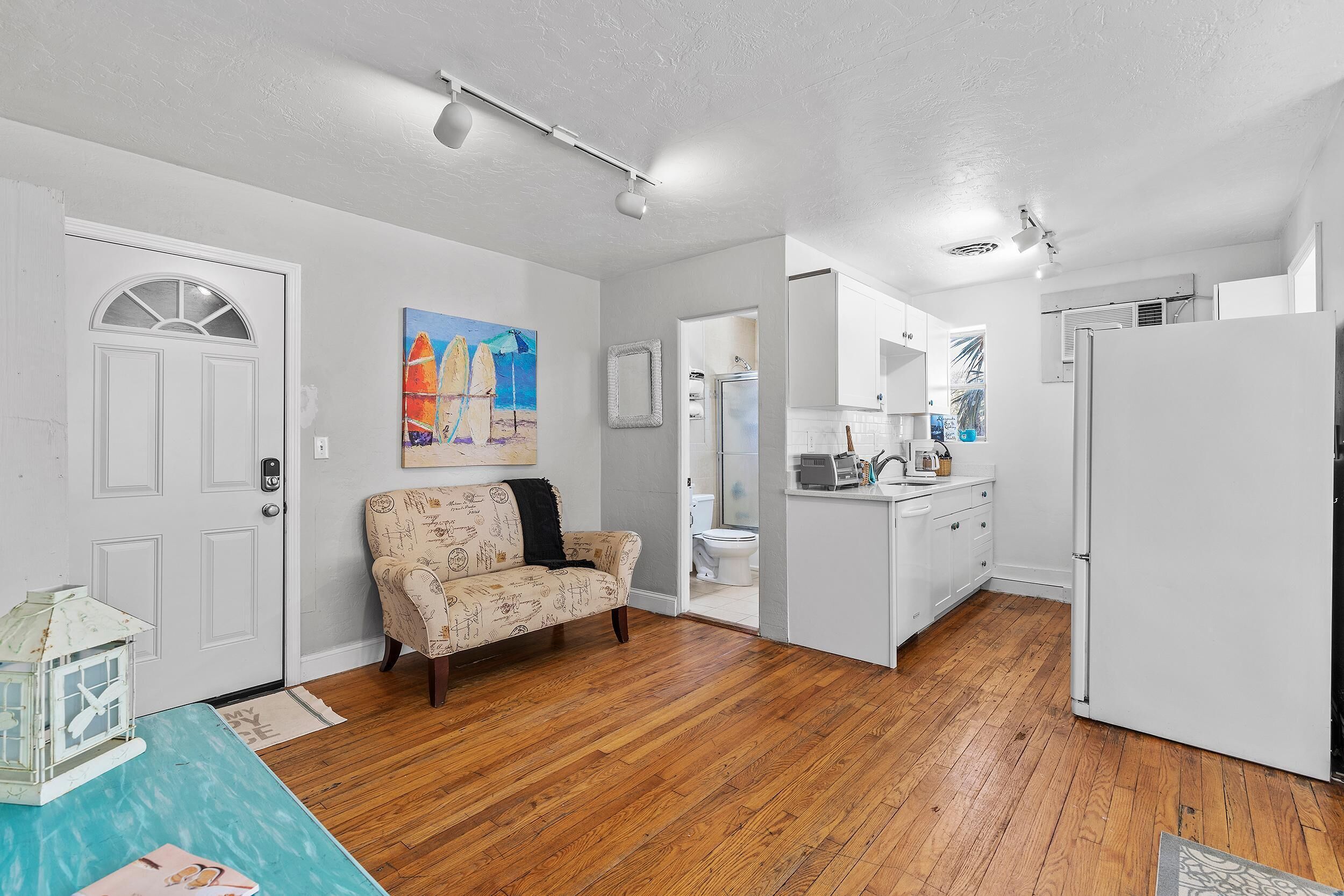 A modern kitchen with white cabinets, a refrigerator, and a dining area with a wooden table and a patterned armchair.