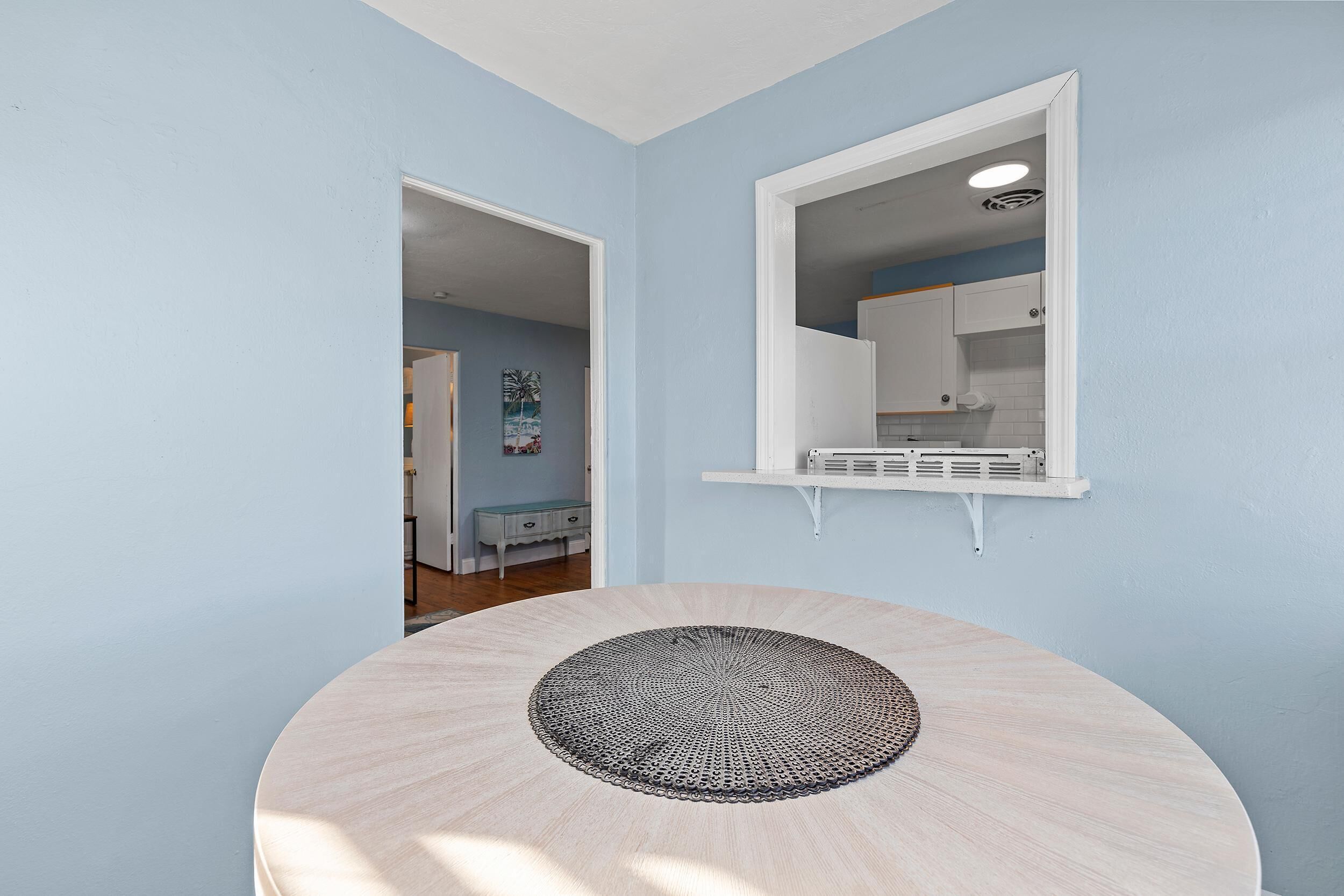Une pièce avec une table ronde, une fenêtre à cadre blanc et un mur bleu clair.