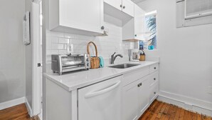 A kitchen with white cabinets, a toaster, a sink, and a window with a view. - Flagler Suites 4 (New Smyrna Beach)