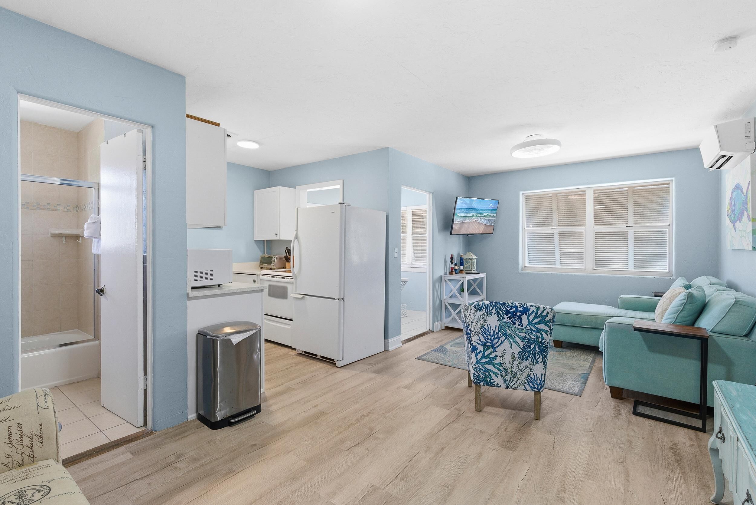 A compact living space with a kitchenette, a sofa, a TV, and a window with blinds.