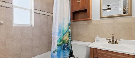 A bathroom with a bathtub, toilet, vanity, and a mirror.