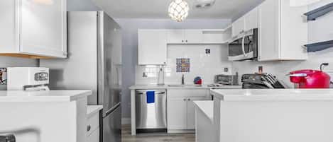Une cuisine moderne avec des meubles blancs, des appareils en acier inoxydable et des luminaires suspendus.