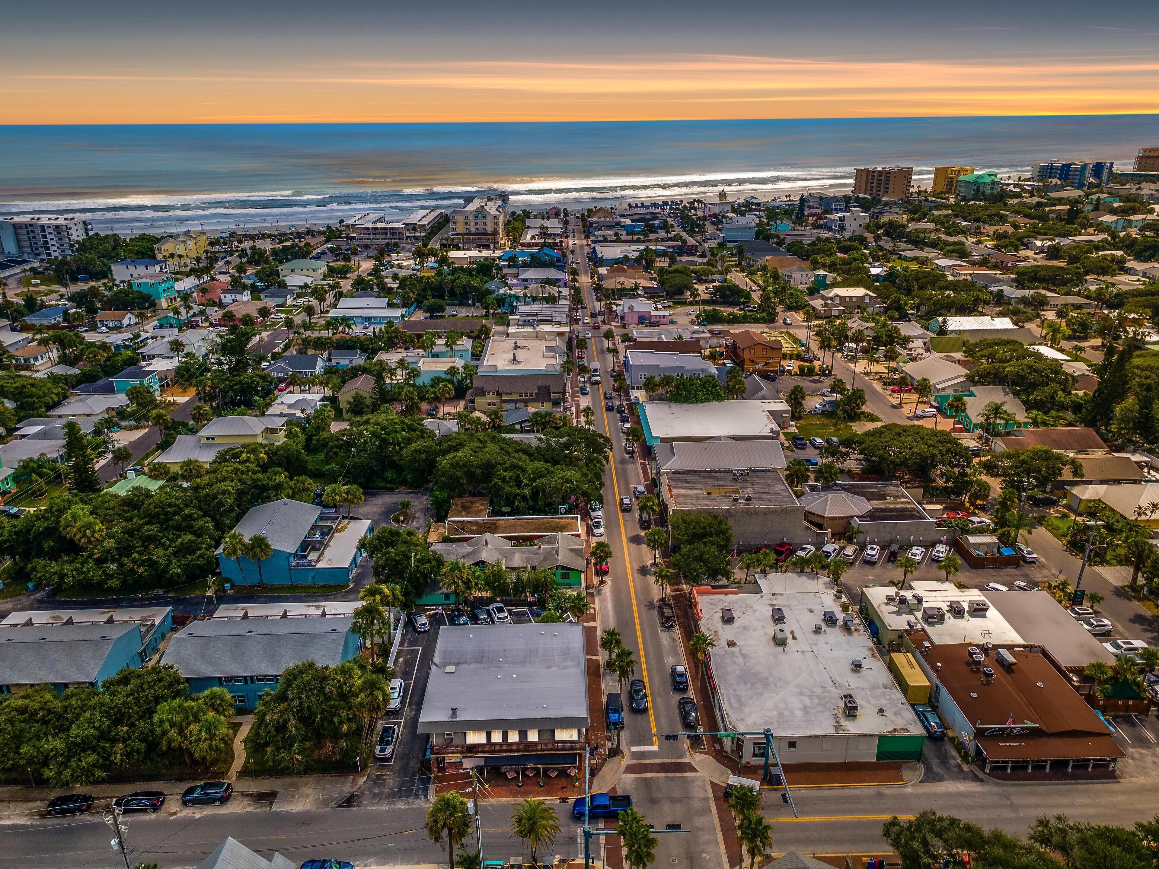 An aerial view of a coastal town with a mix of residential and commercial buildings, a main street, and a view of the ocean.