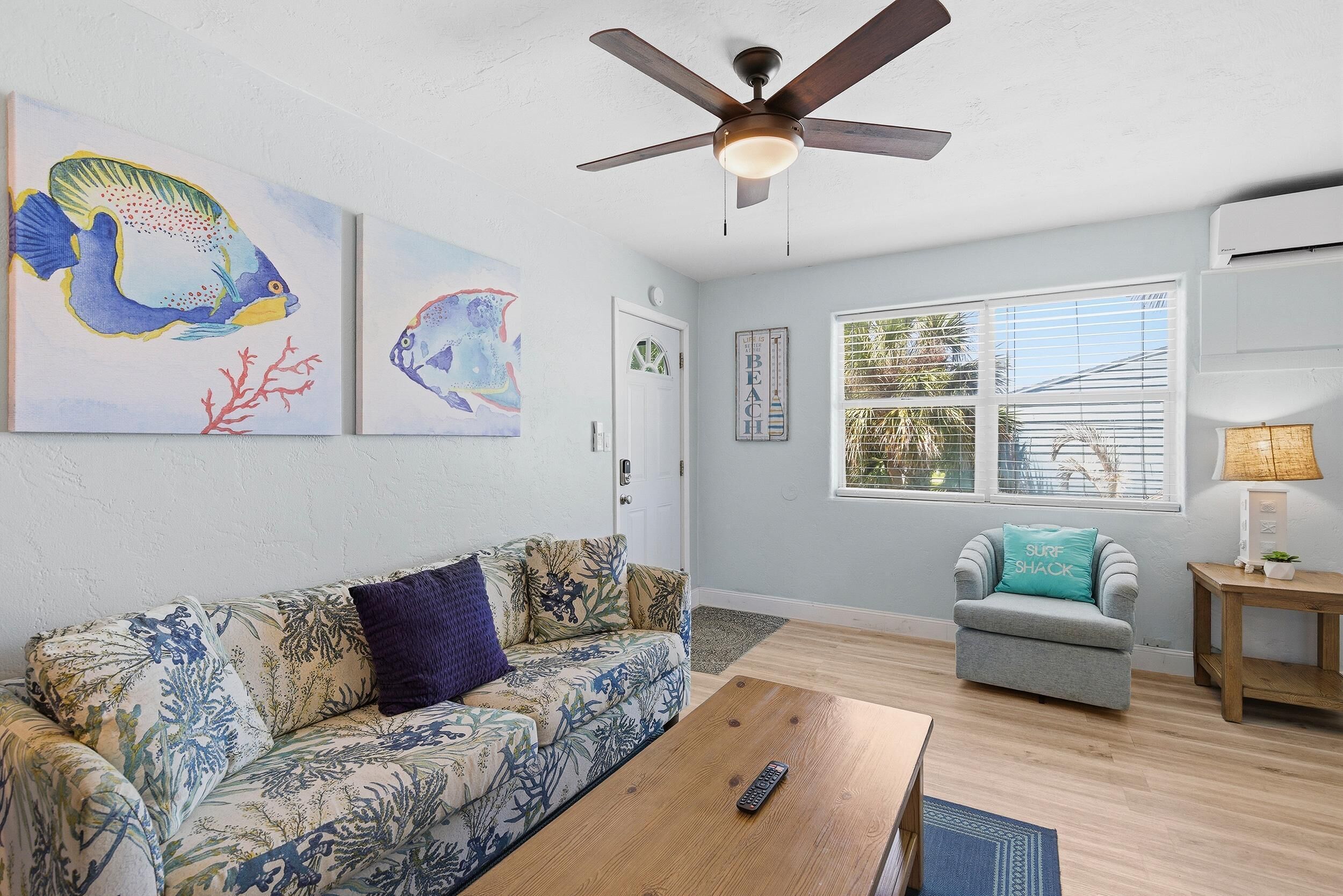 A living room with a ceiling fan, a sofa, a coffee table, and artwork on the walls.