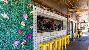 En restaurang med en grön vägg som är dekorerad med blommor, en bardisk och gula barstolar.