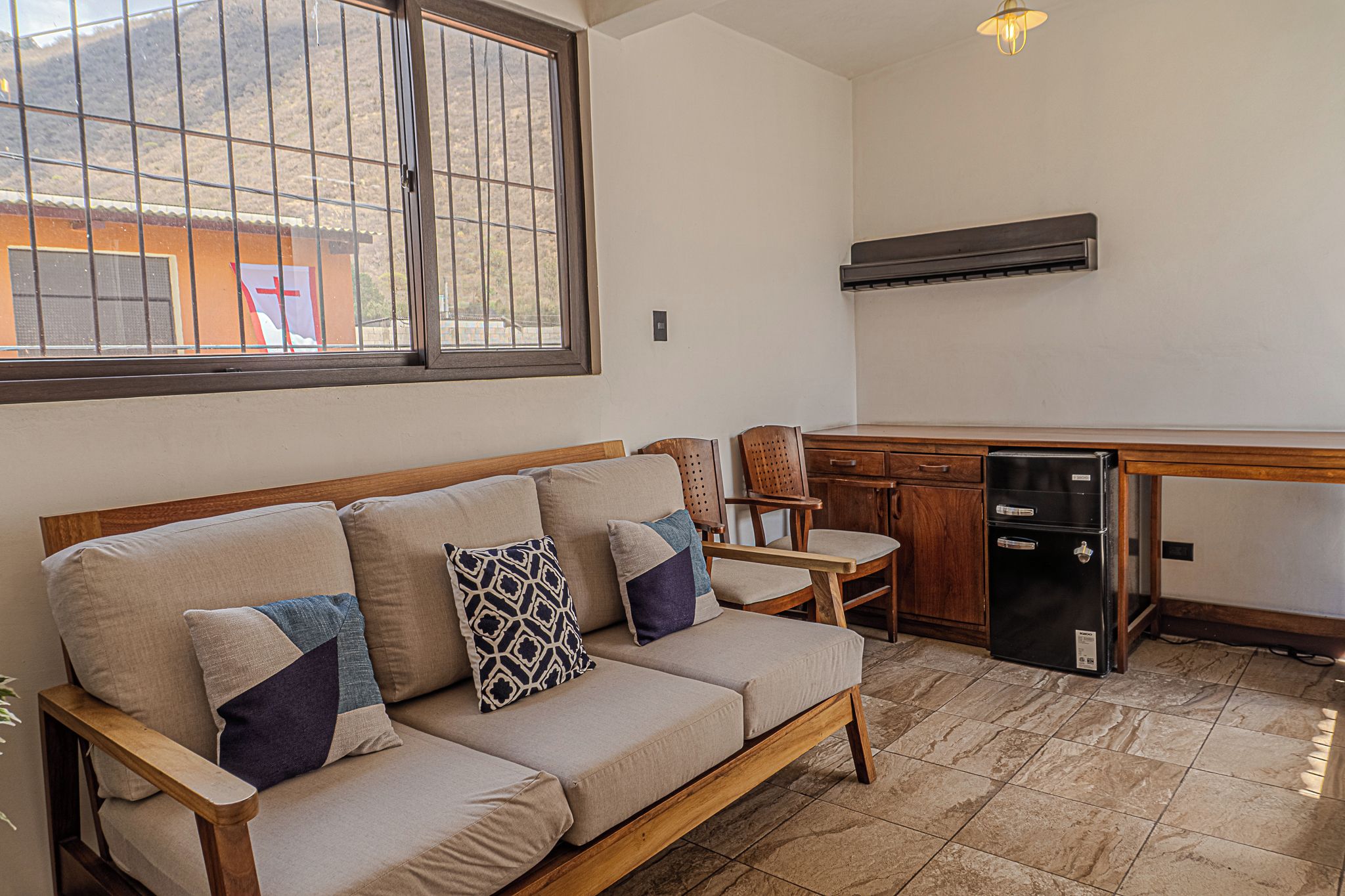 A living area with a sofa, chairs, a small table, and a refrigerator.