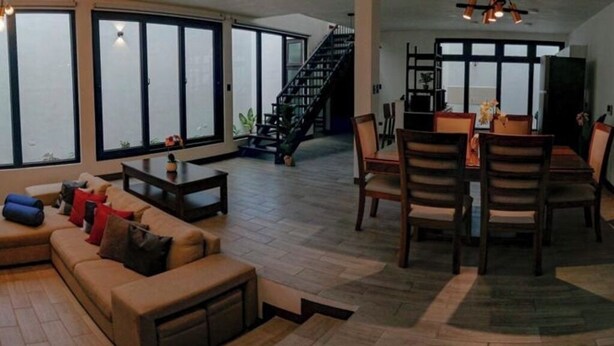 A spacious living area with a sofa, dining table, and chairs. There is a staircase leading to an upper level. - Hermosa casa, con Parqueo propio, Ideal para pasar momentos en familia o pareja. (Jocotenango)