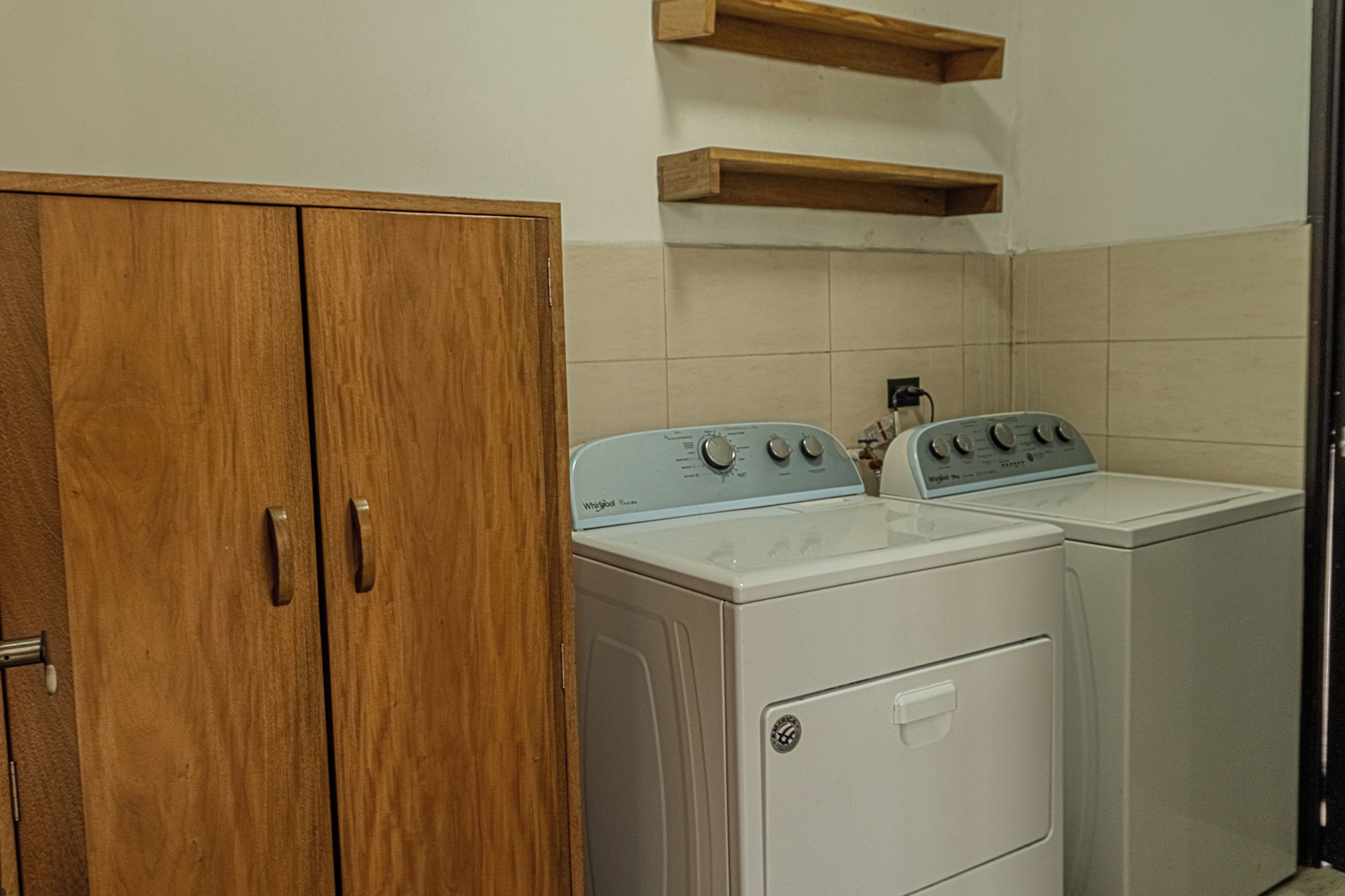 Un espace buanderie avec une armoire en bois et deux machines à laver blanches.