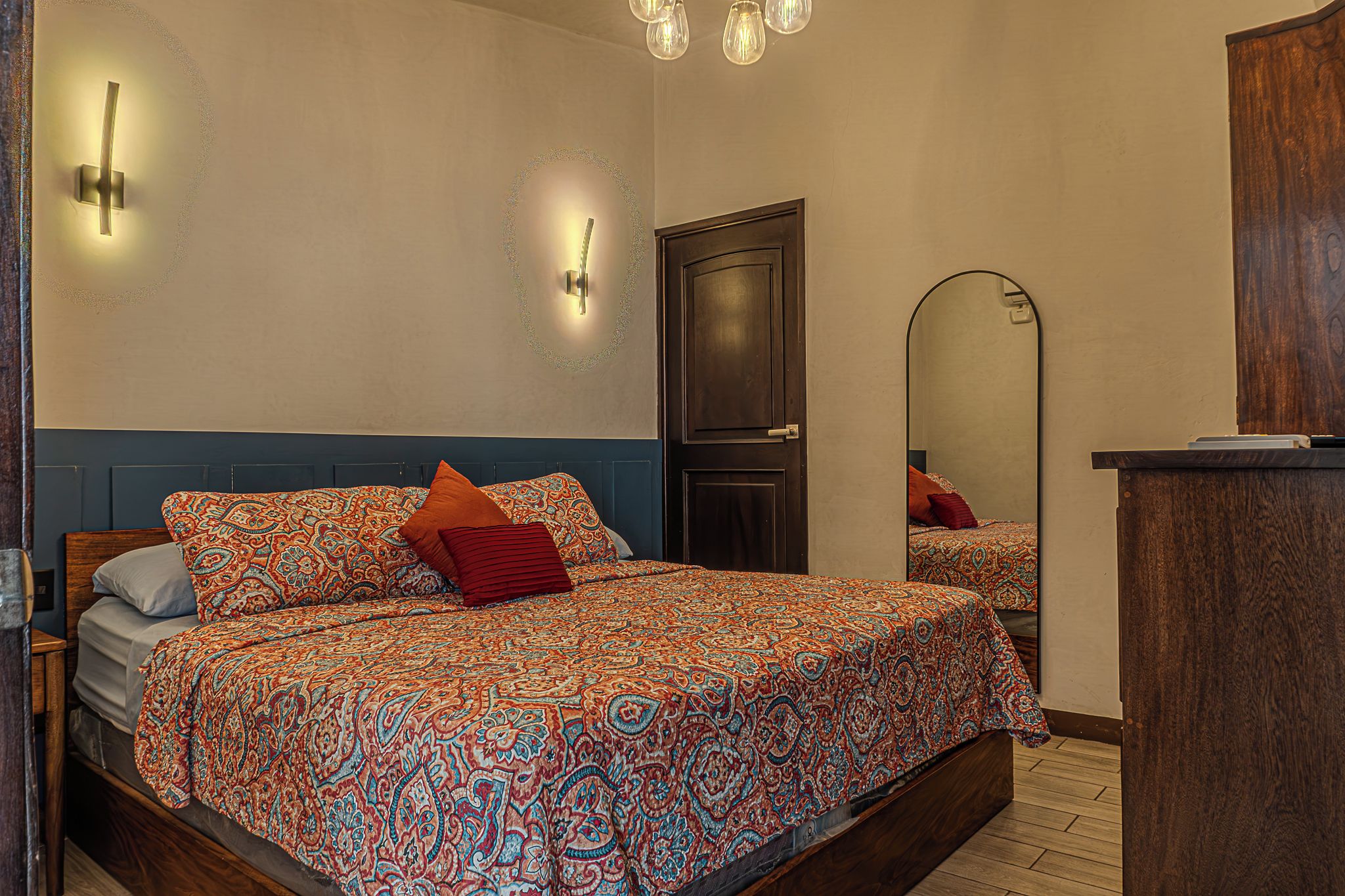 A bedroom with a bed, a dresser, a mirror, and wall sconces.