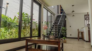 A spacious room with a wooden table, a staircase, and large windows overlooking a garden.