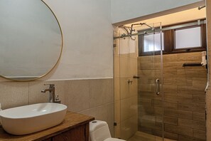 Une salle de bain avec un miroir rond, un lavabo et un espace douche.